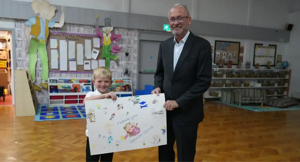 Charlie Spencer stood with a student from Longhill Primary School holding a poster made by the children for Spencer Group